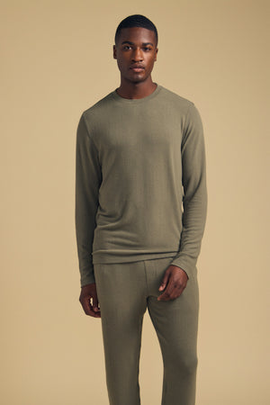 A man stands against a plain beige background, wearing the Velvet by Graham & Spencer REDDEN CREW PULLOVER in olive green paired with matching pants, looking directly at the camera.