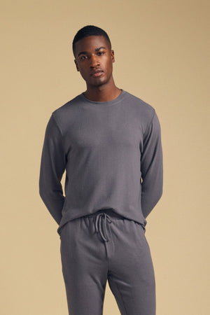 A man wearing the Velvet by Graham & Spencer REDDEN CREW PULLOVER and matching drawstring pants stands against a plain beige background with his hands behind his back.