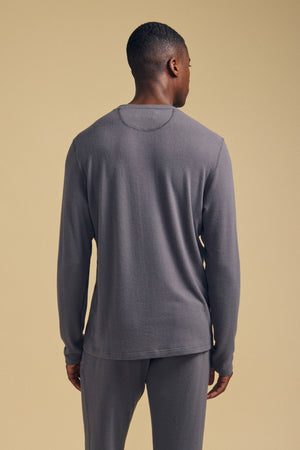 A person stands facing away from the camera, wearing the Velvet by Graham & Spencer REDDEN CREW PULLOVER in gray with matching pants, set against a plain beige background.
