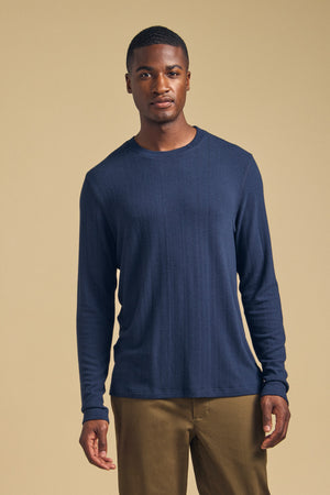 A man wears a cozy, navy blue Velvet by Graham & Spencer REDDEN CREW PULLOVER with brown pants.