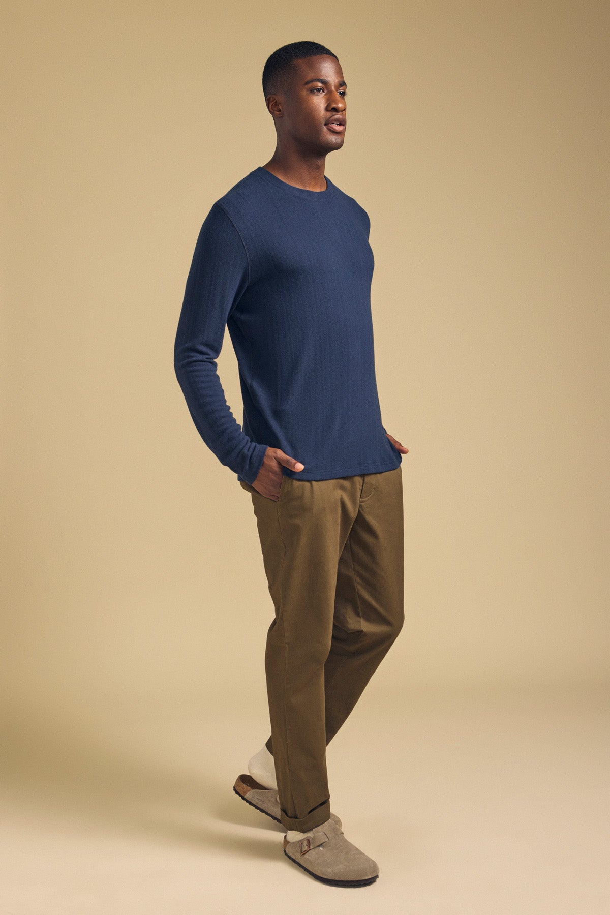A man wearing a blue Velvet by Graham & Spencer REDDEN CREW PULLOVER, olive trousers, and beige slip-on shoes.