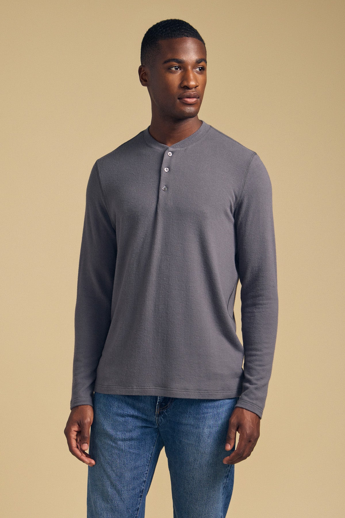 A man wearing the TYLER HENLEY long sleeve shirt by Velvet by Graham & Spencer and blue jeans stands against a plain beige background, looking off to the side.-41859822682305