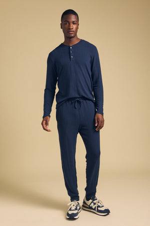 A man wearing a navy long-sleeved TYLER HENLEY by Velvet by Graham & Spencer jersey shirt and matching drawstring joggers.