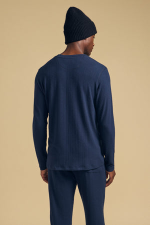 A man seen from behind wearing a navy blue TYLER HENLEY, matching pants, and a dark beanie.