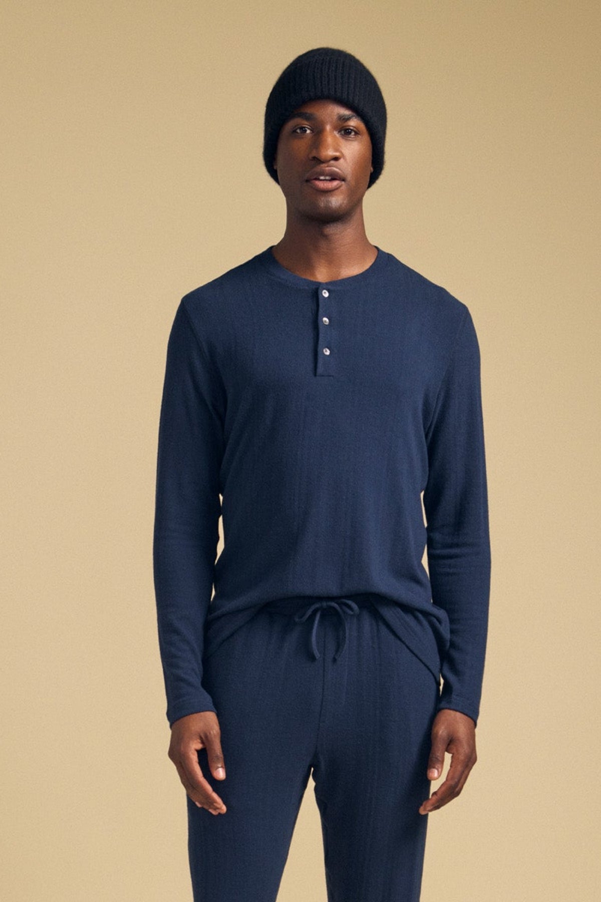 A man wearing a navy blue TYLER HENLEY long-sleeved jersey, matching drawstring pants, and a black beanie.