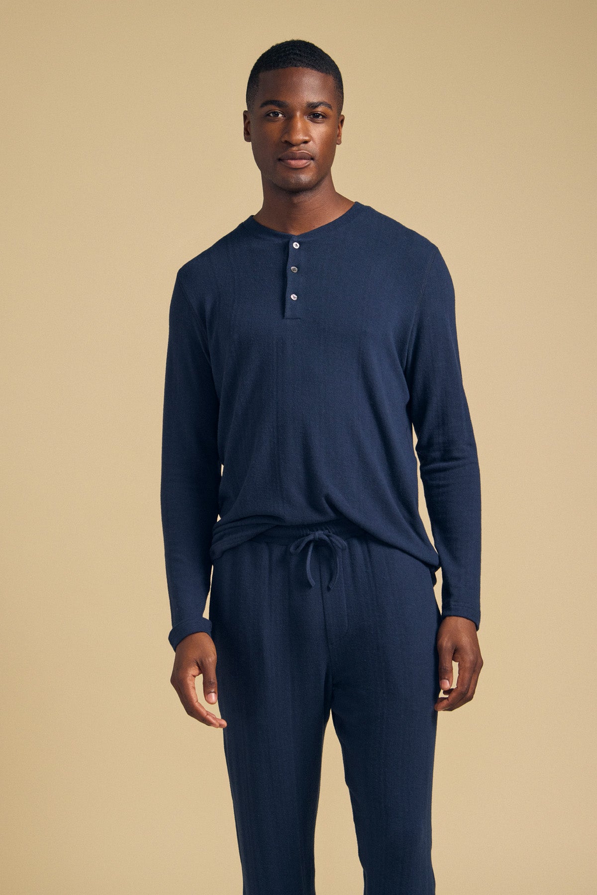 A man wearing the navy blue TYLER HENLEY long-sleeved jersey shirt with a button placket and matching drawstring lounge pants.