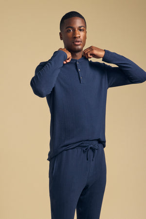 A man wearing a navy blue TYLER HENLEY long-sleeve shirt and matching drawstring pants.
