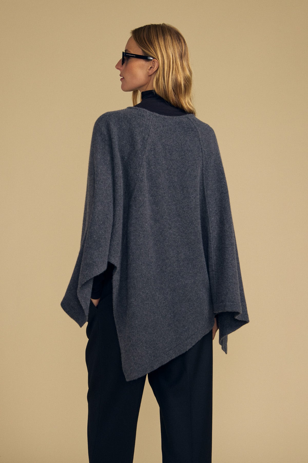 A person wearing the GIA PONCHO by Velvet by Graham & Spencer over dark pants and a black top stands facing away from the camera against a plain beige background.