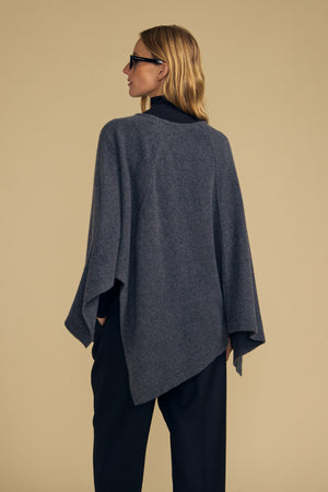 A person wearing the GIA PONCHO by Velvet by Graham & Spencer over dark pants and a black top stands facing away from the camera against a plain beige background.