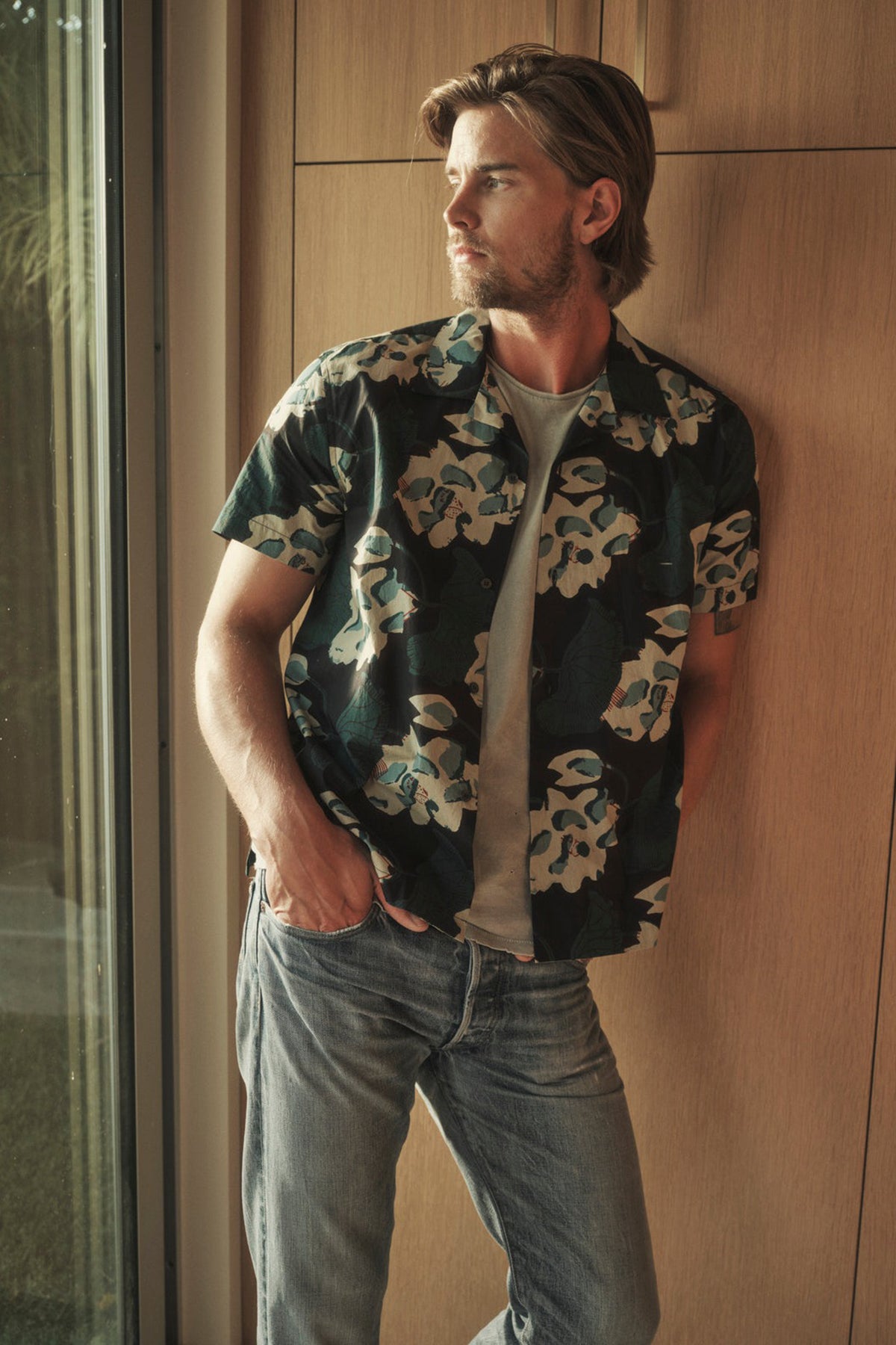  A man in the Velvet by Graham & Spencer Iggy Printed Button-Up Shirt leaning against a window. 