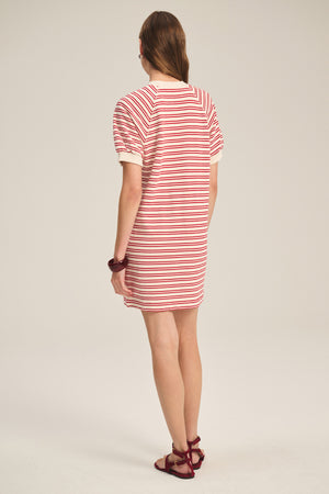 A person faces away, wearing the Velvet by Graham & Spencer DARCIE DRESS—vintage-inspired with red and white stripes—paired with red sandals, light brown hair, and a red bracelet.