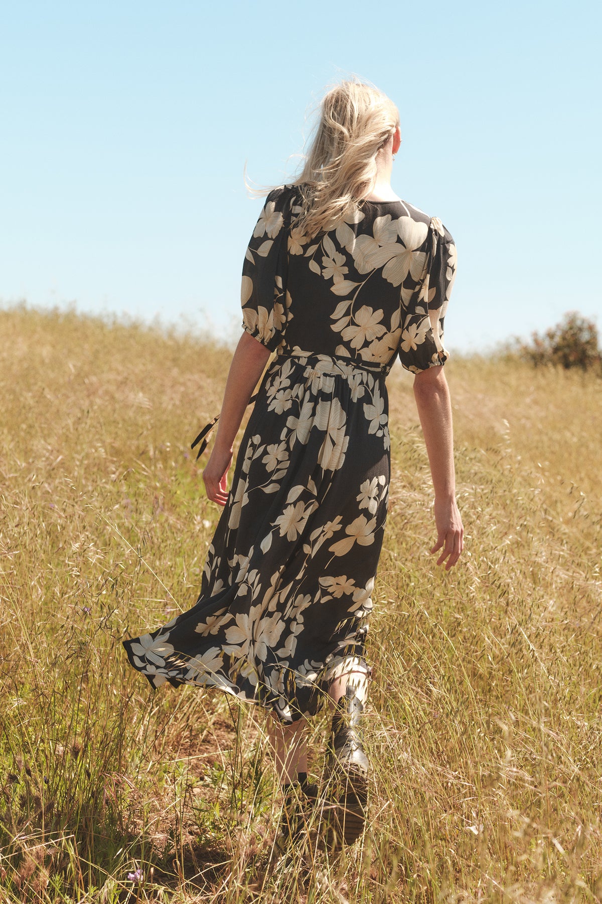   A woman walking through tall grass in a Velvet by Graham & Spencer KAI PRINTED WRAP DRESS. 
