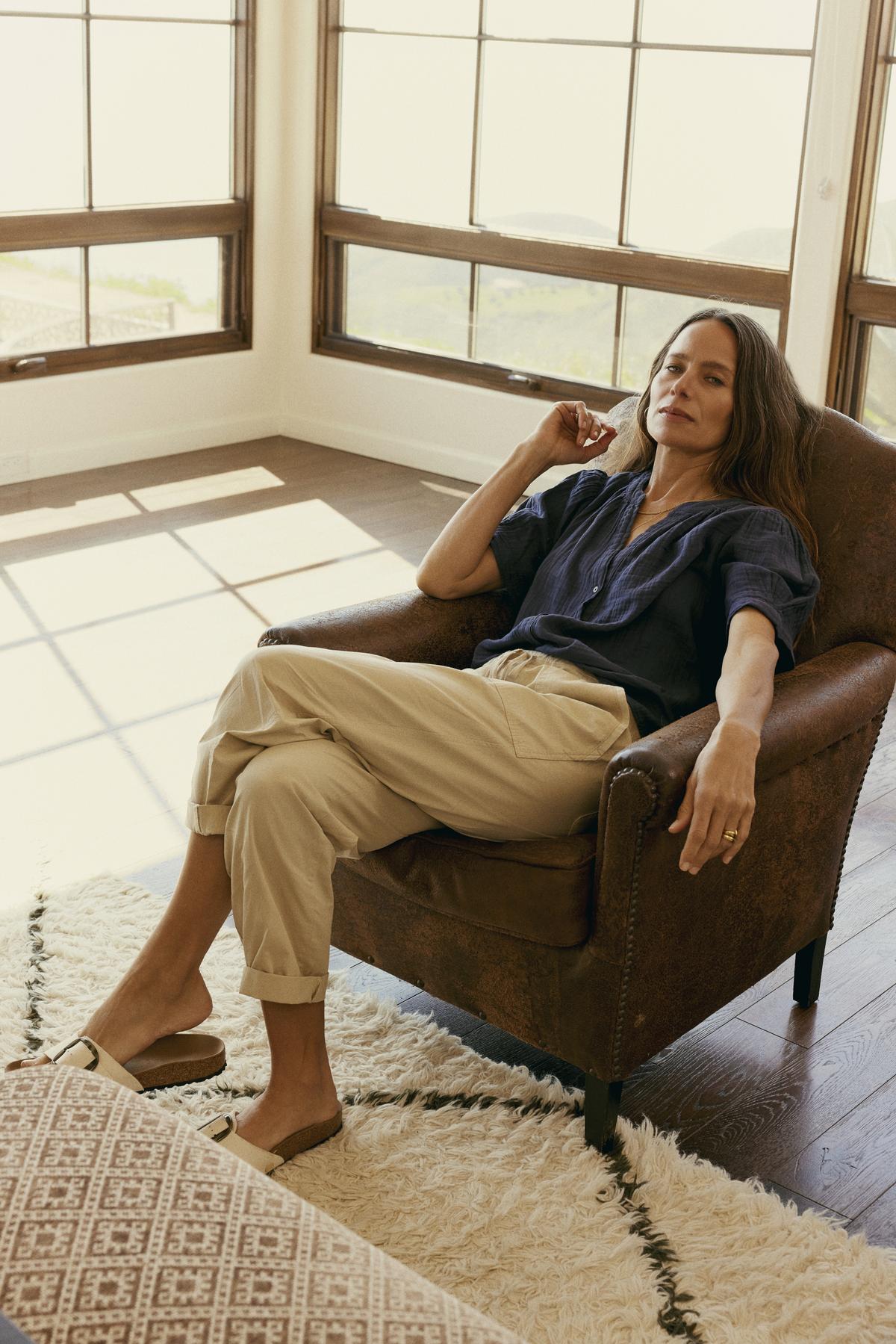   Woman relaxing in a leather armchair in a sunny room with large windows, wearing Velvet by Graham & Spencer's Misty Cotton Twill Pant. 