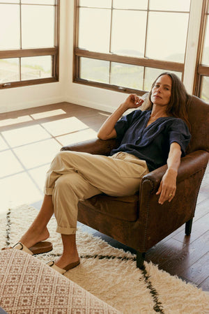 Woman relaxing in a leather armchair in a sunny room with large windows, wearing Velvet by Graham & Spencer's Misty Cotton Twill Pant.