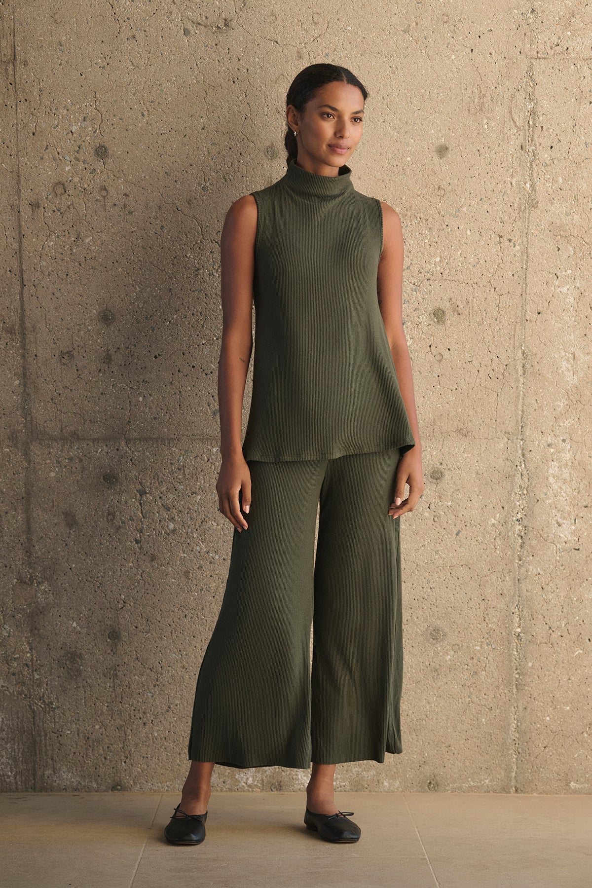 A person stands against a concrete wall wearing the KRYSTAL RIBBED TOP by Velvet by Graham & Spencer, along with matching wide-legged pants and black shoes.-38282006757569