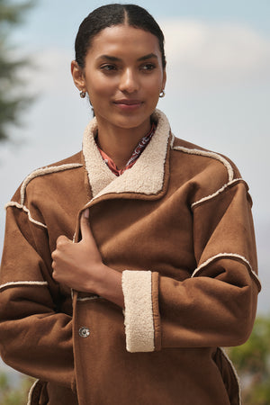 Wearing the ALBANY LUXE SHERPA REVERSIBLE JACKET by Velvet by Graham & Spencer, a person stands outdoors with a neutral expression.