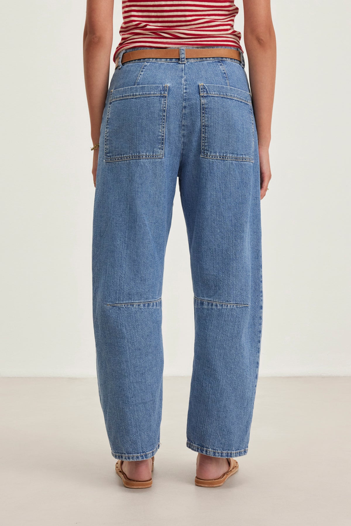   Someone wearing a red and white striped top, Velvet by Graham & Spencer's FARAH DENIM PANT with large back pockets, a brown belt, and sandals, standing on a light surface. 