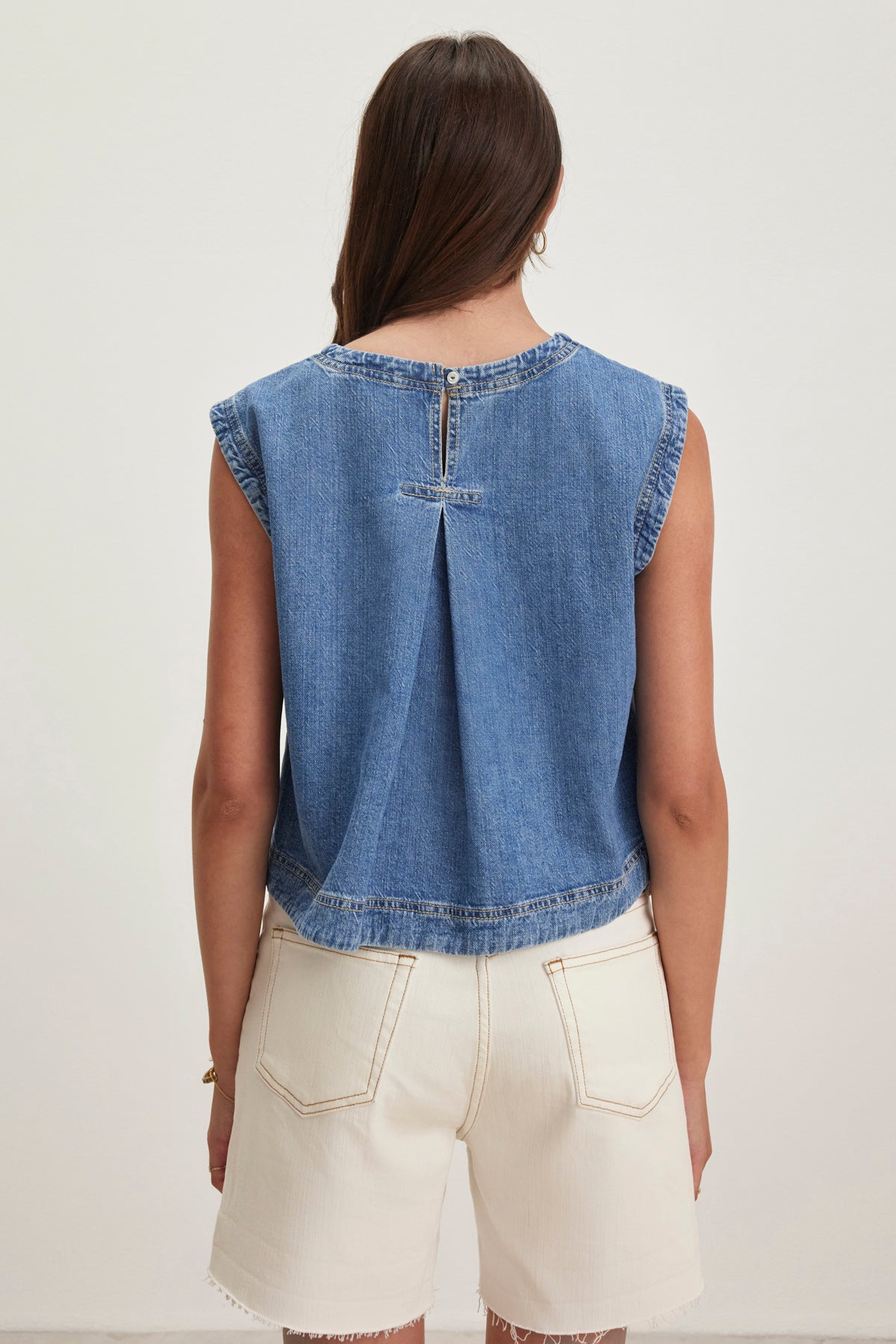 Back view of a person with long hair wearing the LOREN DENIM TOP by Velvet by Graham & Spencer and cream shorts against a plain background.-38820684136641