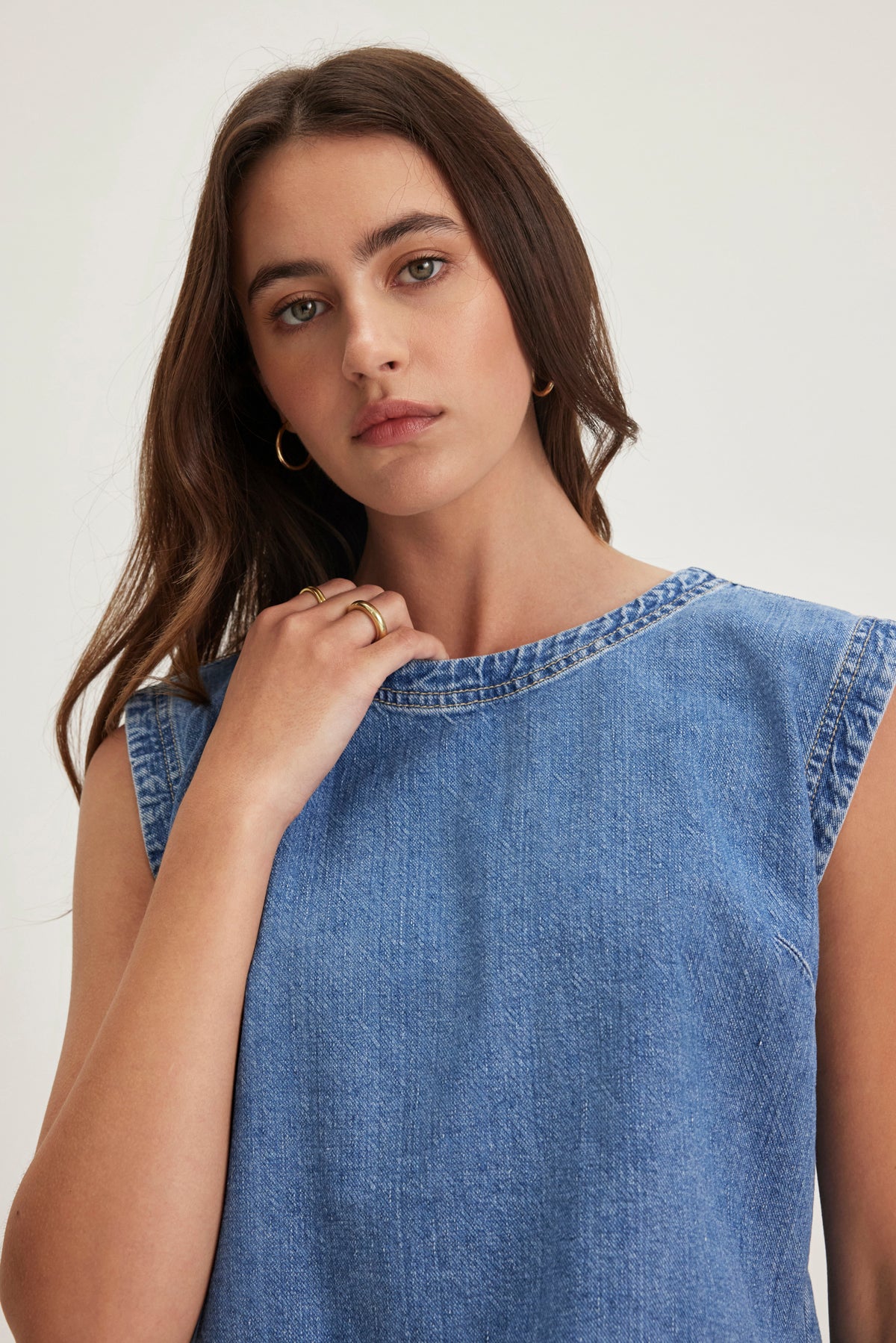 A person with long brown hair wears the LOREN DENIM TOP by Velvet by Graham & Spencer, styled with gold hoop earrings and a neutral expression.-38820684038337