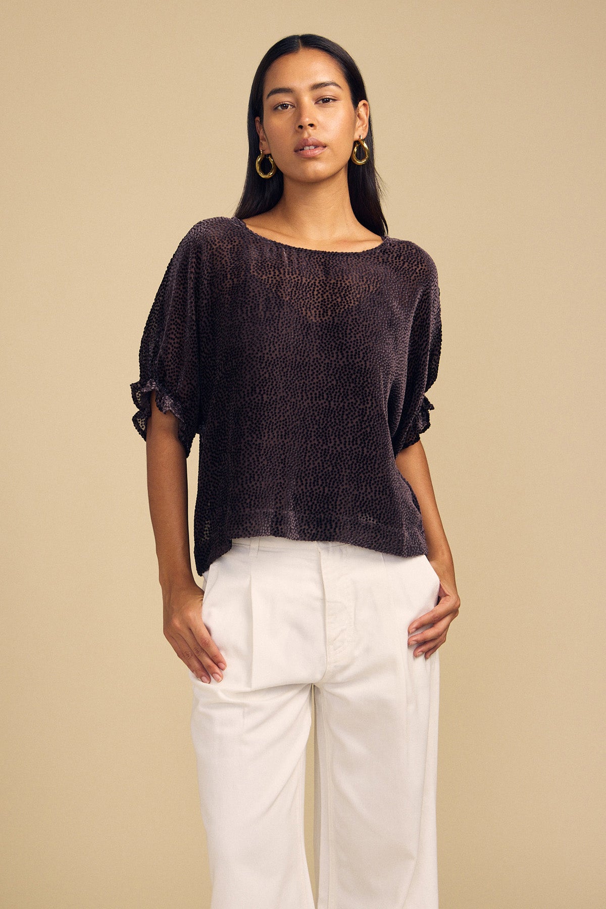 A model wears a dark, short-sleeved burnout texture ADDIE DEVORE DOT BLOUSE by Velvet by Graham & Spencer with white pleated trousers.-46488075763905