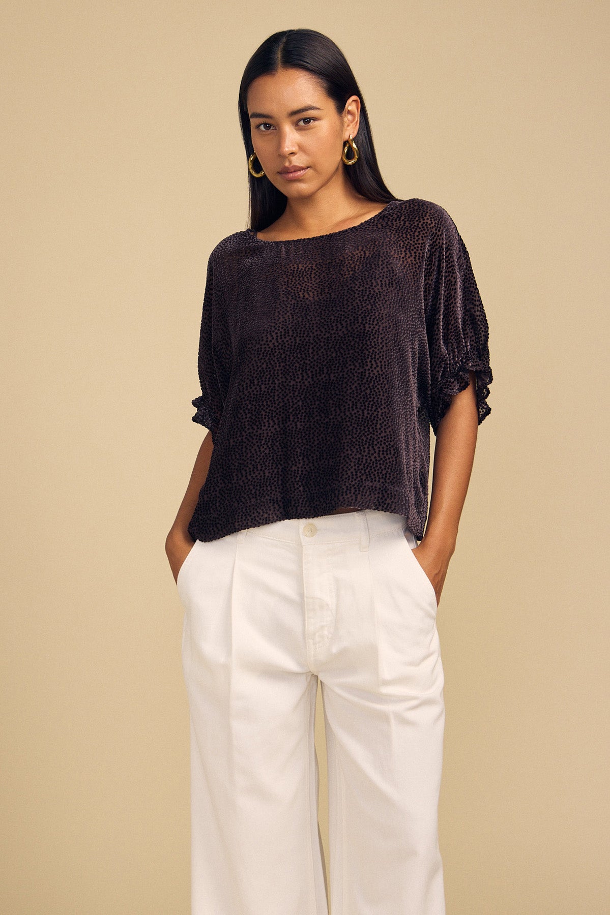 A woman wearing a dark, short-sleeved burnout texture ADDIE DEVORE DOT BLOUSE and white wide-leg trousers.-46488075796673