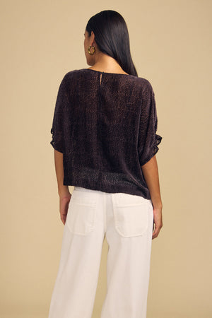 A person seen from behind wears the dark brown, short-sleeved, dot-patterned burnout texture ADDIE DEVORE DOT BLOUSE with white trousers.