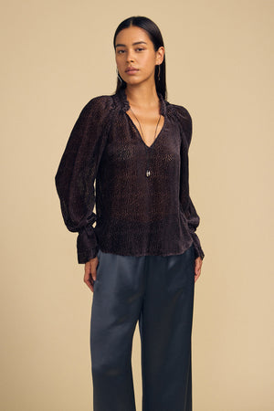 A woman wearing a dark brown, long-sleeved Velvet by Graham & Spencer EMERSON DEVORE DOT BLOUSE with a delicate dot pattern, a V-neckline, and gathered cuffs.
