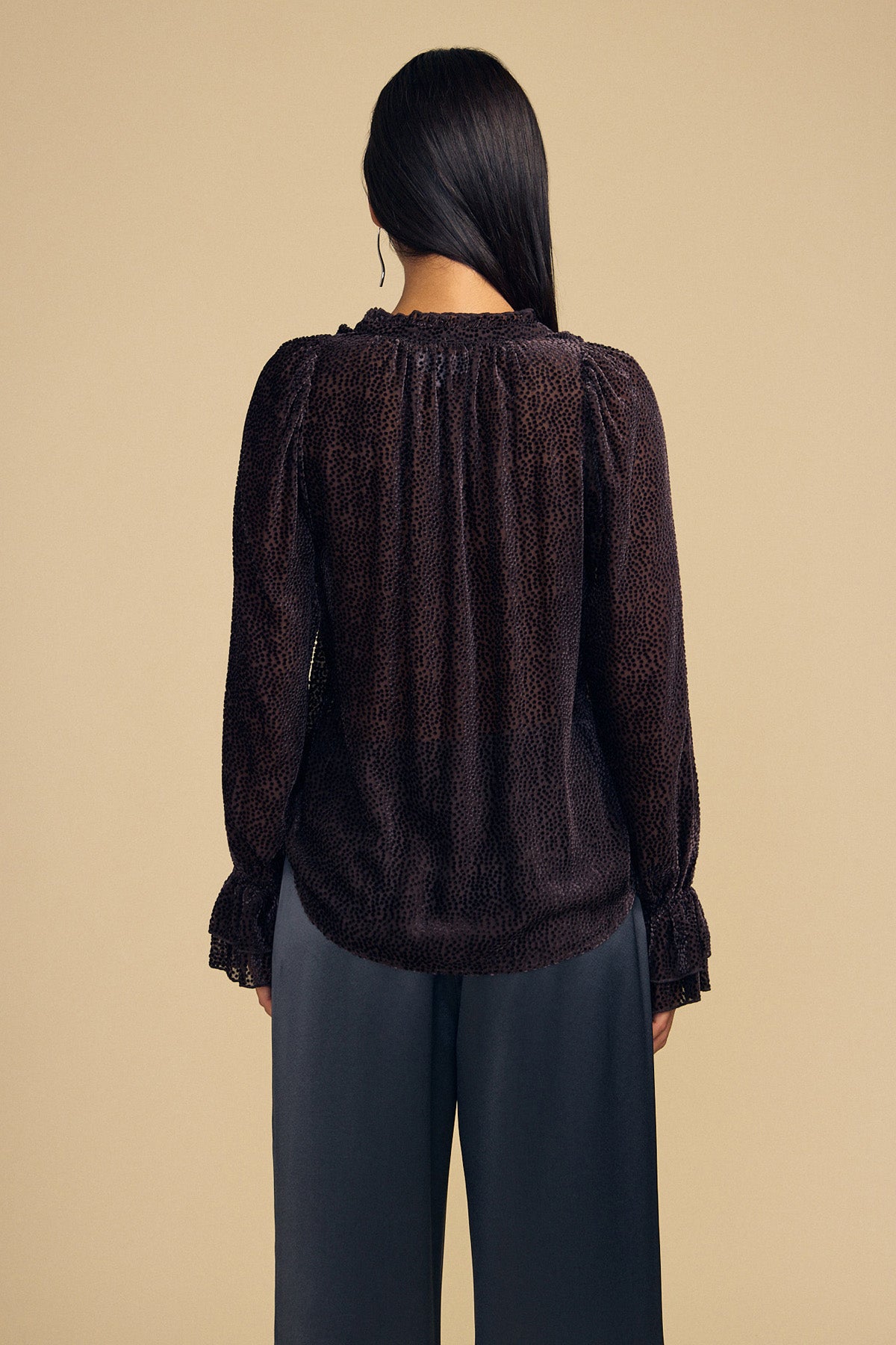 Back view of a person wearing the dark brown silk EMERSON DEVORE DOT BLOUSE with a flocked dot pattern, a ruffled collar, and ruffled cuffs.