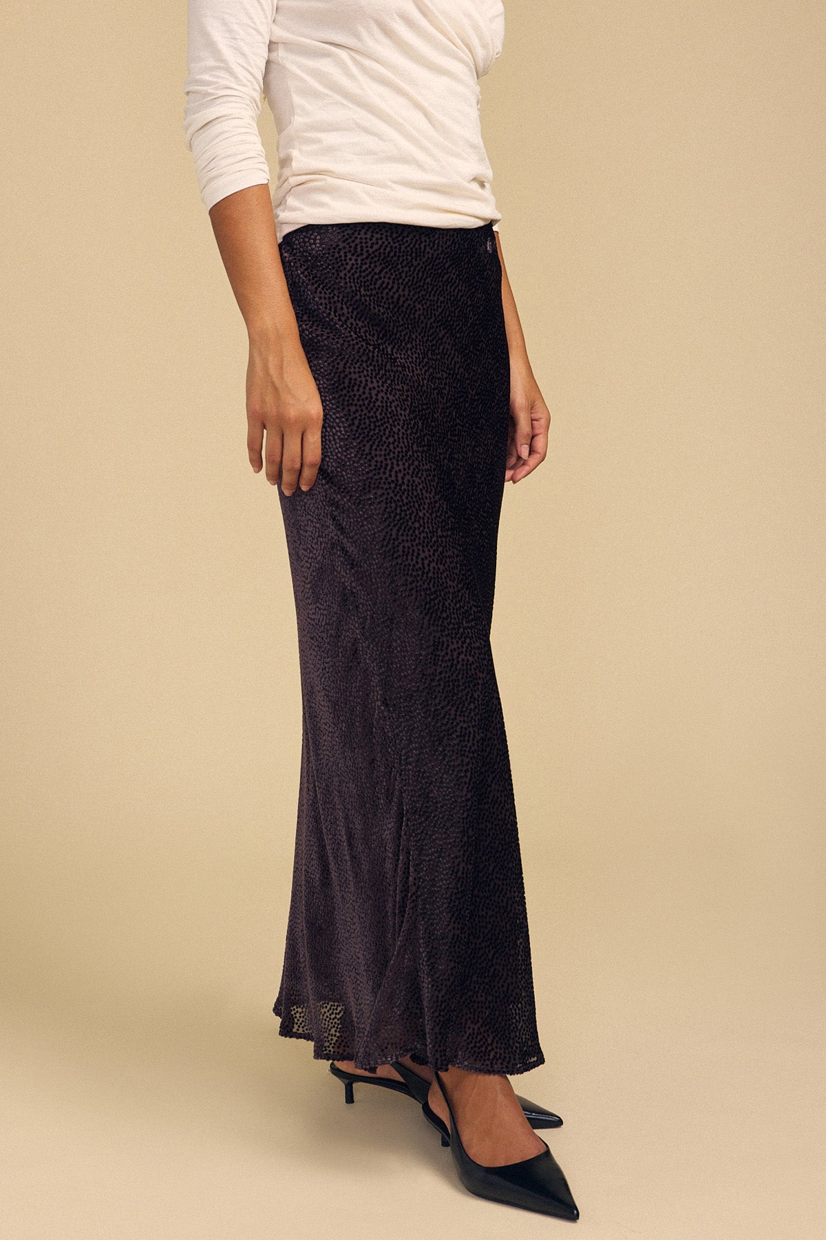 A person wearing a QUINN DEVORE DOT SKIRT, a white long-sleeved top, and black pointed-toe heels.