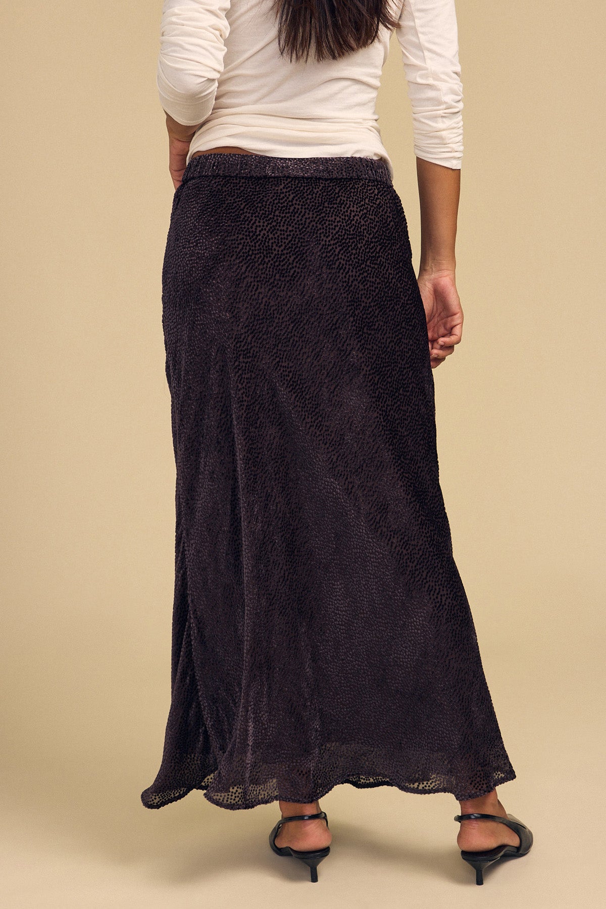 A person seen from behind wears a white long-sleeved top and the dark, bias-cut burnout QUINN DEVORE DOT SKIRT by Velvet by Graham & Spencer.