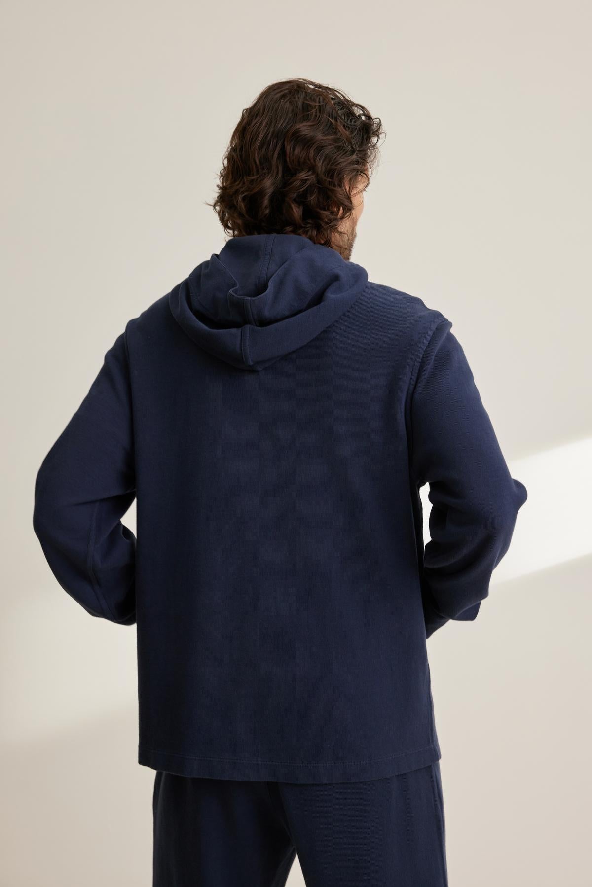 A person with curly hair facing away wears a navy blue MORTY HOODIE by Velvet by Graham & Spencer and matching pants against a neutral background.-38643326877889