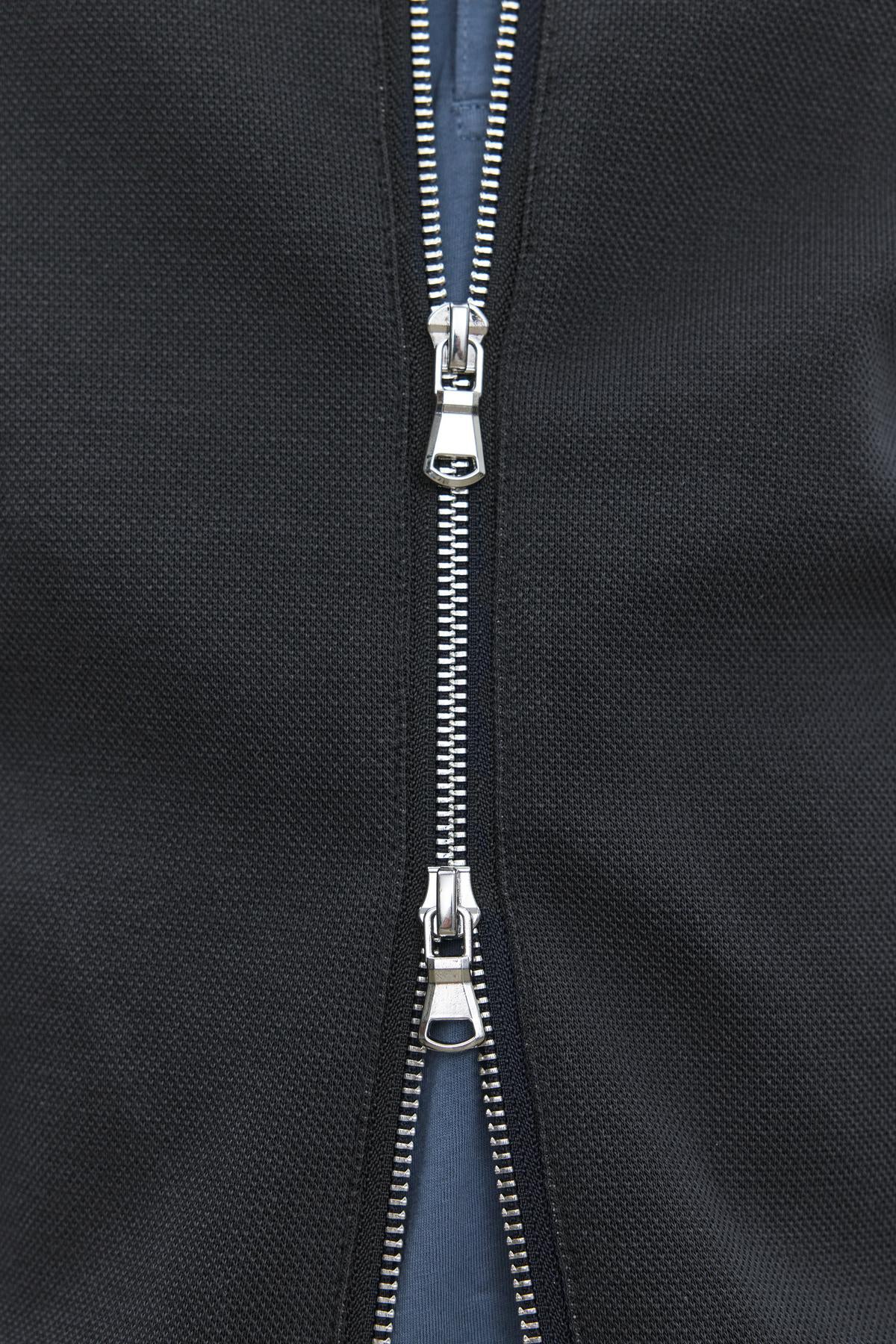   Close-up of the partially opened double zipper on the RYDELL JACKET by Velvet by Graham & Spencer, highlighting the metal teeth and two slider pull tabs against the black textured cotton blend fabric. 