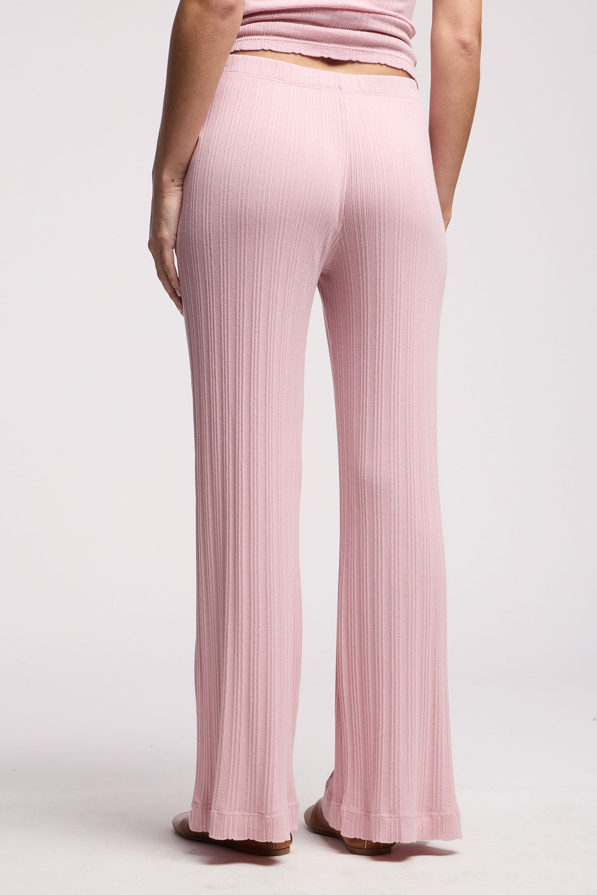 A person is seen from the back wearing Velvet by Graham & Spencer's ALEMI POINTELLE PANT—light pink, high-waisted, flared leg cotton-modal pants with ribbed details—against a plain background.-40416877576385