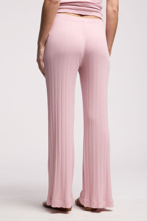 A person is seen from the back wearing Velvet by Graham & Spencer's ALEMI POINTELLE PANT—light pink, high-waisted, flared leg cotton-modal pants with ribbed details—against a plain background.