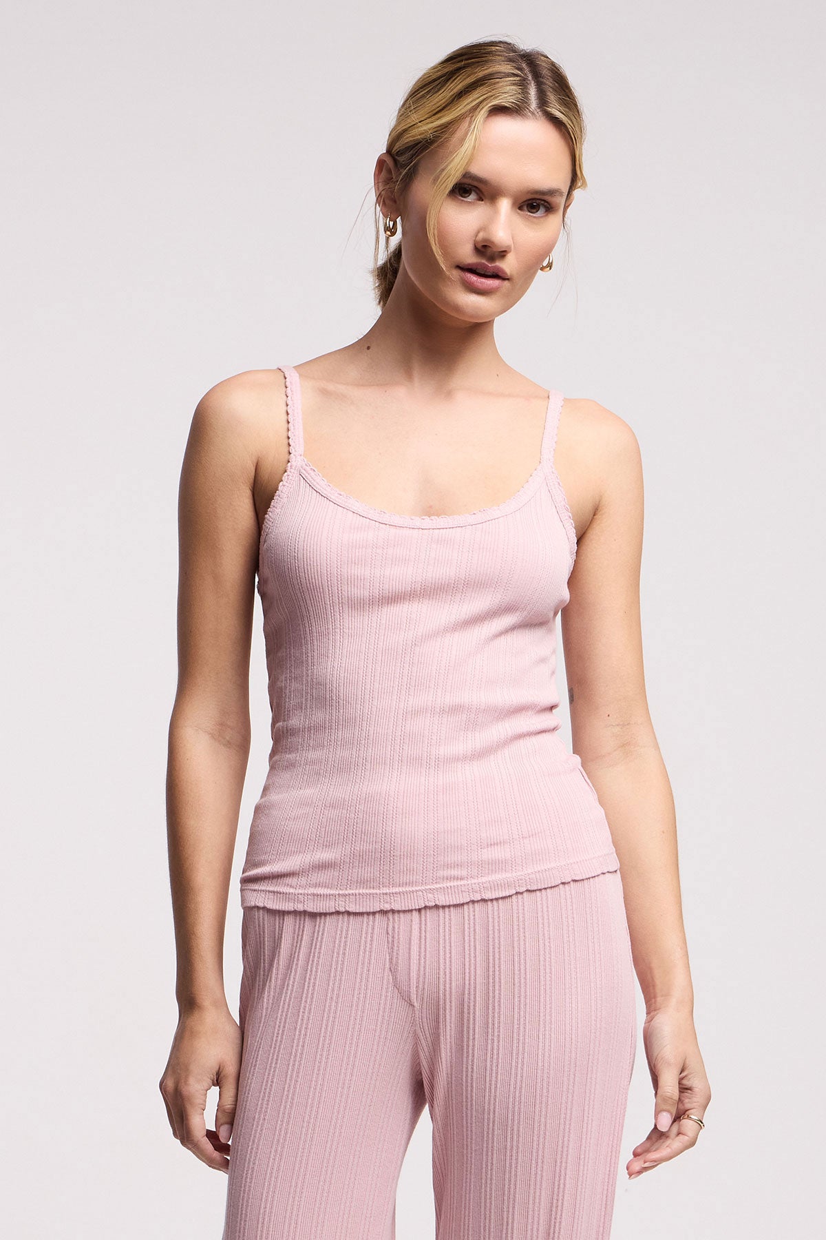 A woman faces forward against a plain light background, wearing the INIKU POINTELLE TANK TOP by Velvet by Graham & Spencer in light pink with ribbed texture and matching pants.
