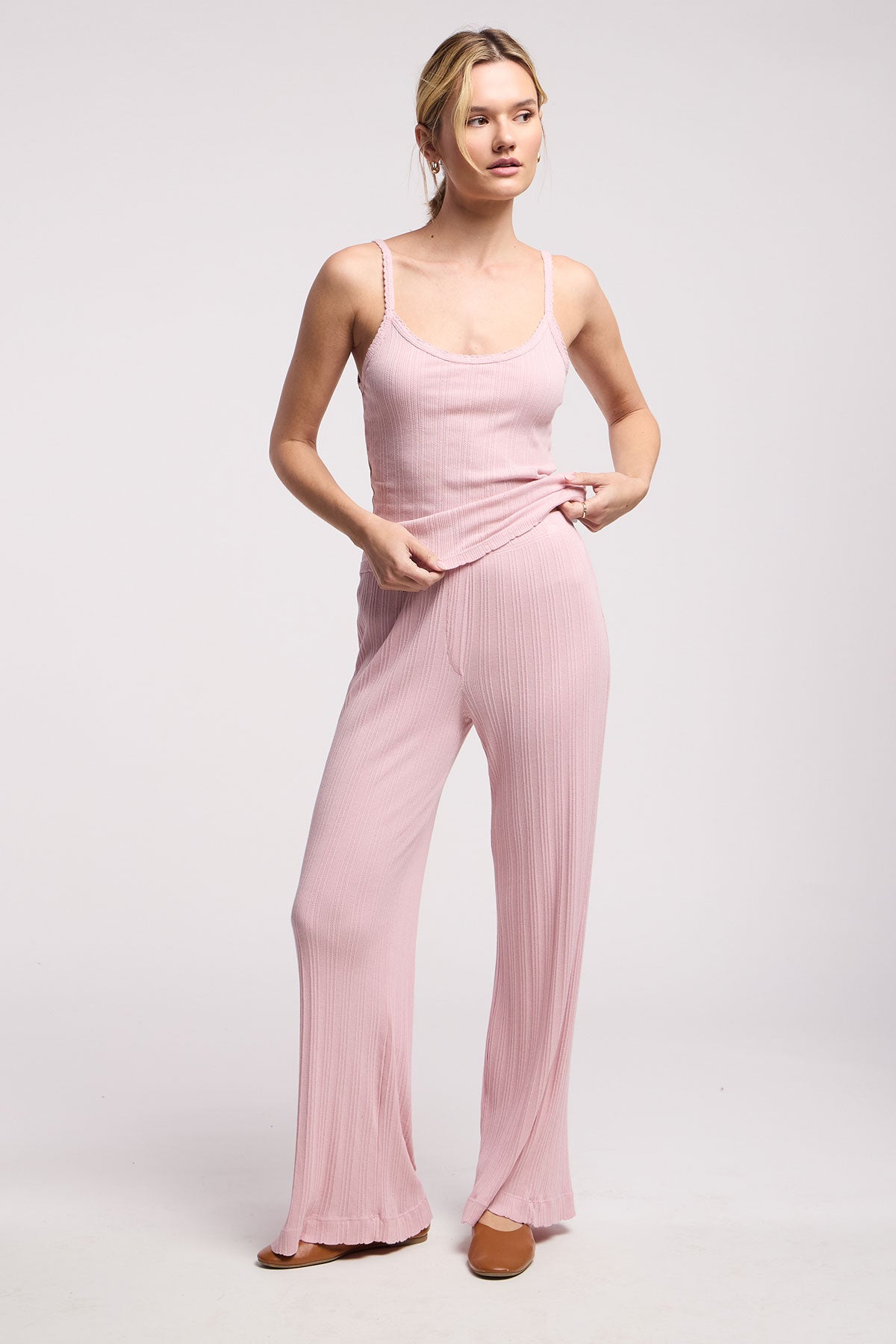 A woman stands against a plain background wearing Velvet by Graham & Spencer’s ALEMI POINTELLE PANT, a light pink sleeveless ribbed top, and flat shoes.