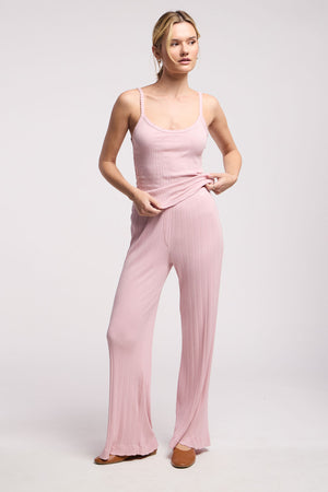A woman stands against a plain background wearing Velvet by Graham & Spencer’s ALEMI POINTELLE PANT, a light pink sleeveless ribbed top, and flat shoes.