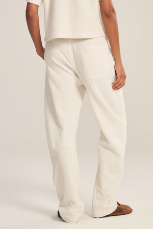 A person faces away from the camera in Velvet by Graham & Spencer's ELISE SWEATPANT, featuring a relaxed white fit, matched with a coordinating top and brown shoes against a simple background.