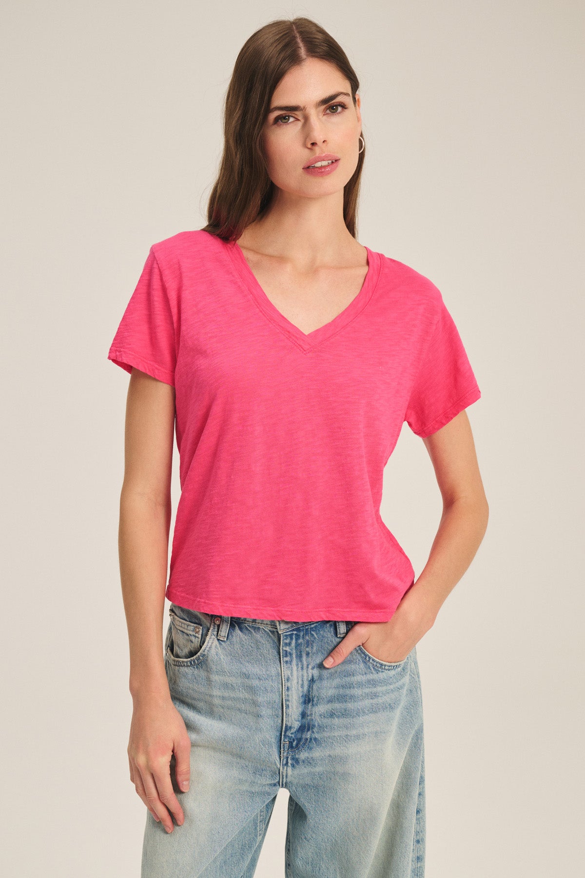 A woman models the ELISHA TEE by Velvet by Graham & Spencer—a bright pink cotton slub V-neck tee—paired with light blue jeans against a plain background for a fresh, modern look.