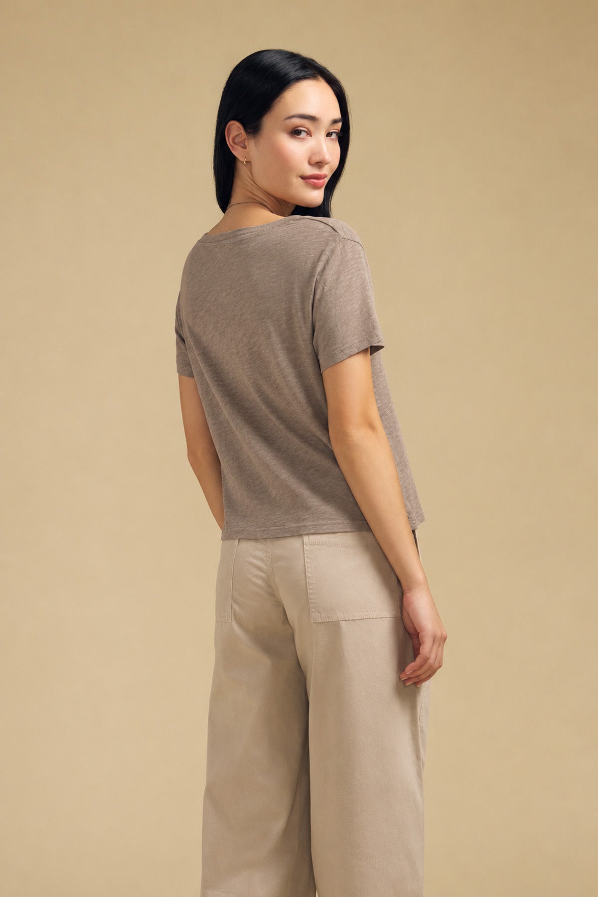 A woman wears a taupe short-sleeved cotton slub ELISHA TEE by Velvet by Graham & Spencer and beige trousers, a versatile wardrobe staple.-46490611777729