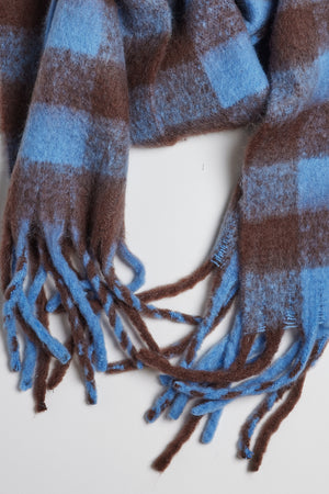 A classic Velvet by Graham & Spencer plaid scarf with fringe ends, the ELLE PLAID SCARF offers warmth and comfort in shades of blue and brown.