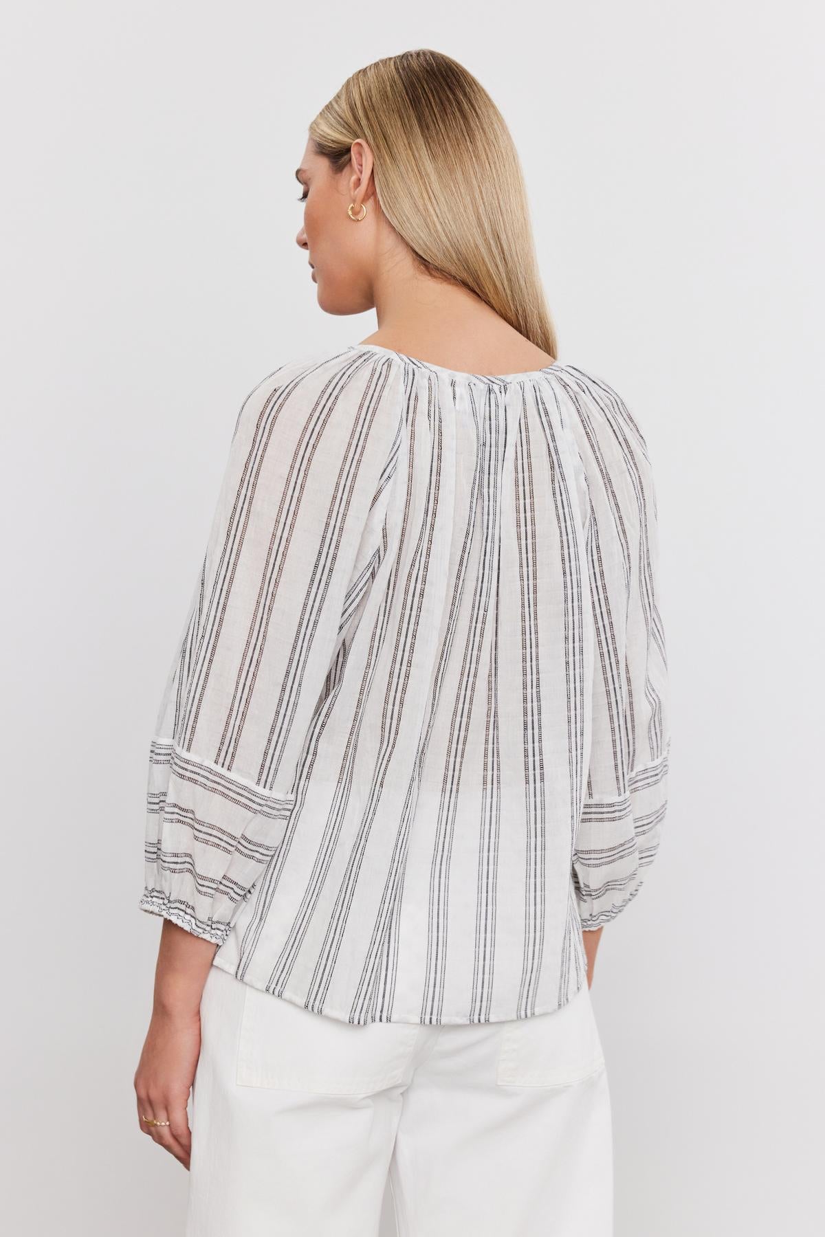 Woman from the back wearing a Gianna Top by Velvet by Graham & Spencer with gathered detailing and white, relaxed fit pants, standing against a plain background.-36910245970113