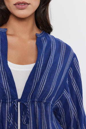 Close-up of a woman wearing a RENATA TOP by Velvet by Graham & Spencer with a drawstring neckline, over a white top.