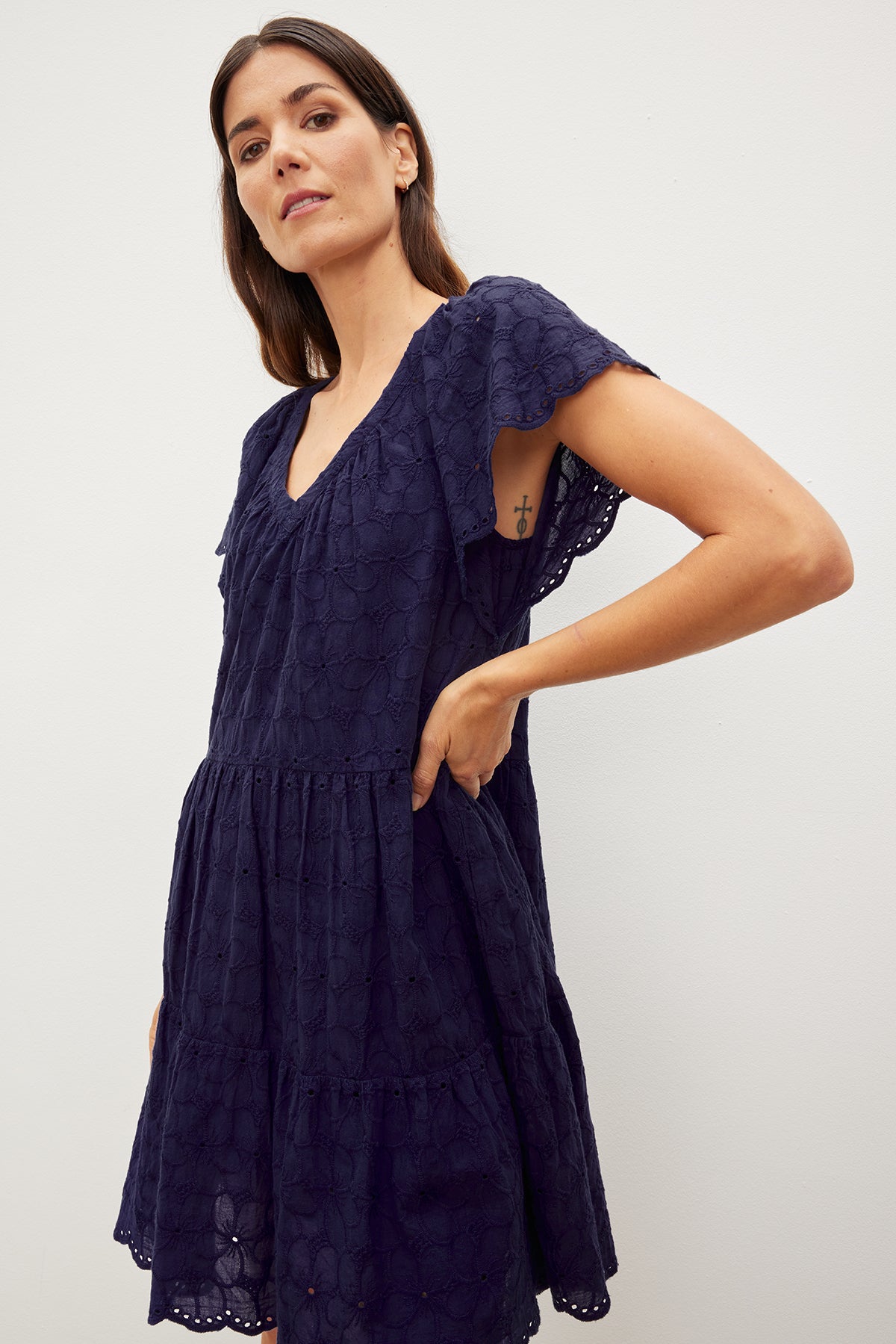 The model is wearing a Velvet by Graham & Spencer WYNETTE EMBROIDERED COTTON DRESS with flutter sleeves and a ruffled hem.-35967521587393