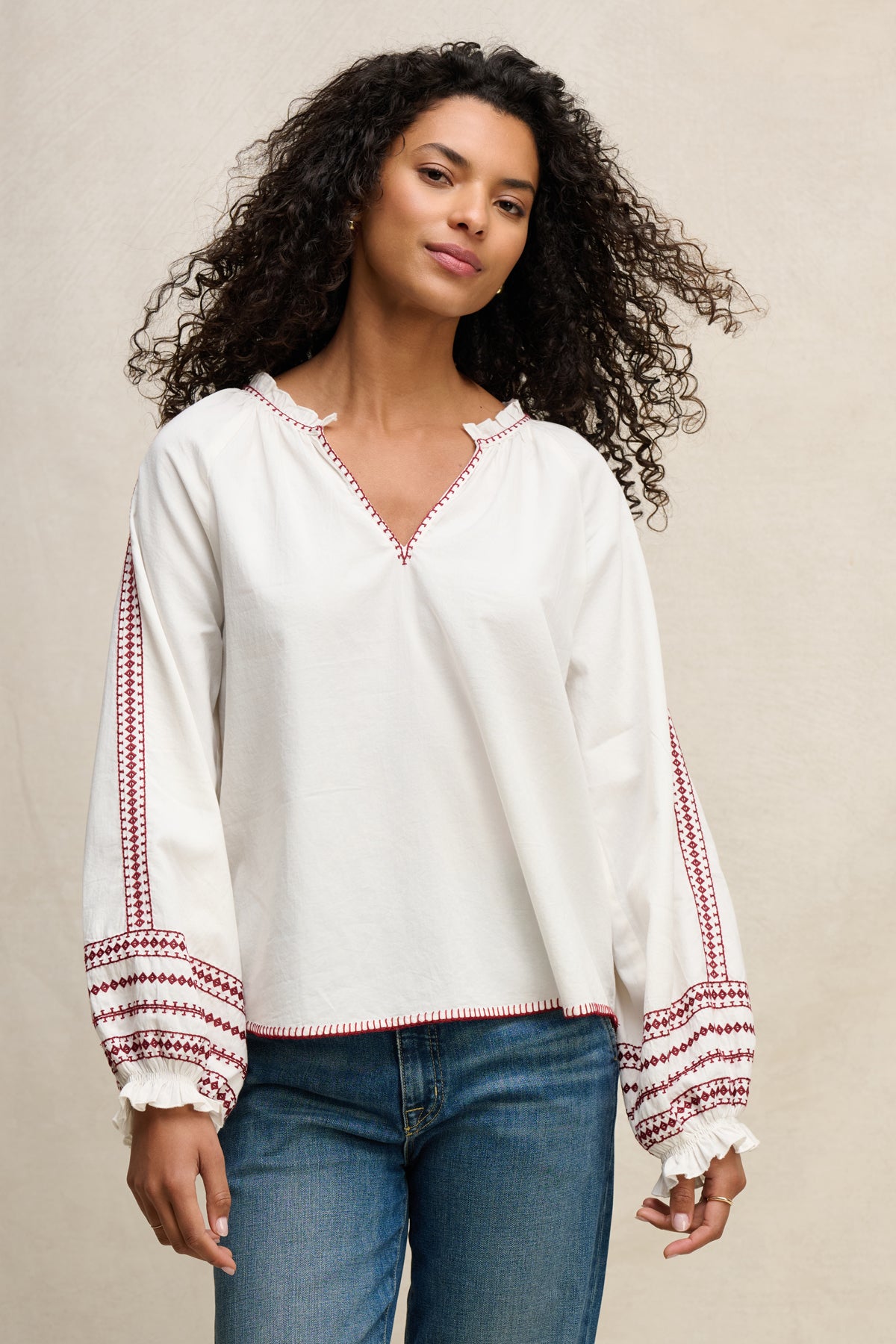 A woman with curly hair wears the SCARLETT TOP by Velvet by Graham & Spencer, a white puff sleeve top, with blue jeans.-39617777402049