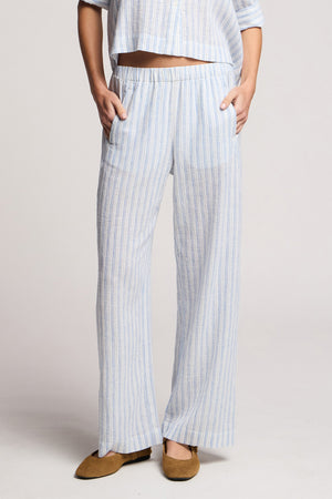 Model wears the EVONY PANT by Velvet by Graham & Spencer, featuring light blue and white vertical stripes, a wide-leg silhouette, and side pockets, paired with tan flats and a matching top.