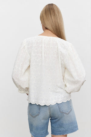 The back view of a woman wearing a Velvet by Graham & Spencer CORINA EMBROIDERED COTTON TOP and denim shorts.