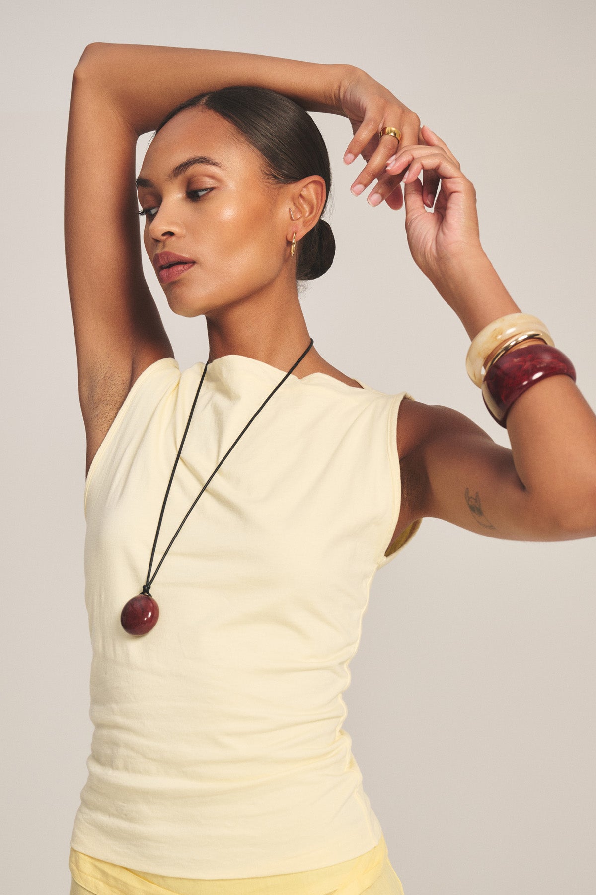 A person wears the EMILIA TANK TOP in yellow by Velvet by Graham & Spencer, paired with matching yellow pants and jewelry, posing with arms raised against a plain background.