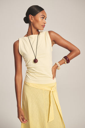 A woman stands looking to the side, wearing the EMILIA TANK TOP by Velvet by Graham & Spencer with a matching skirt, pendant necklace, and stacked bangles—a look as airy as a summertime whisper.