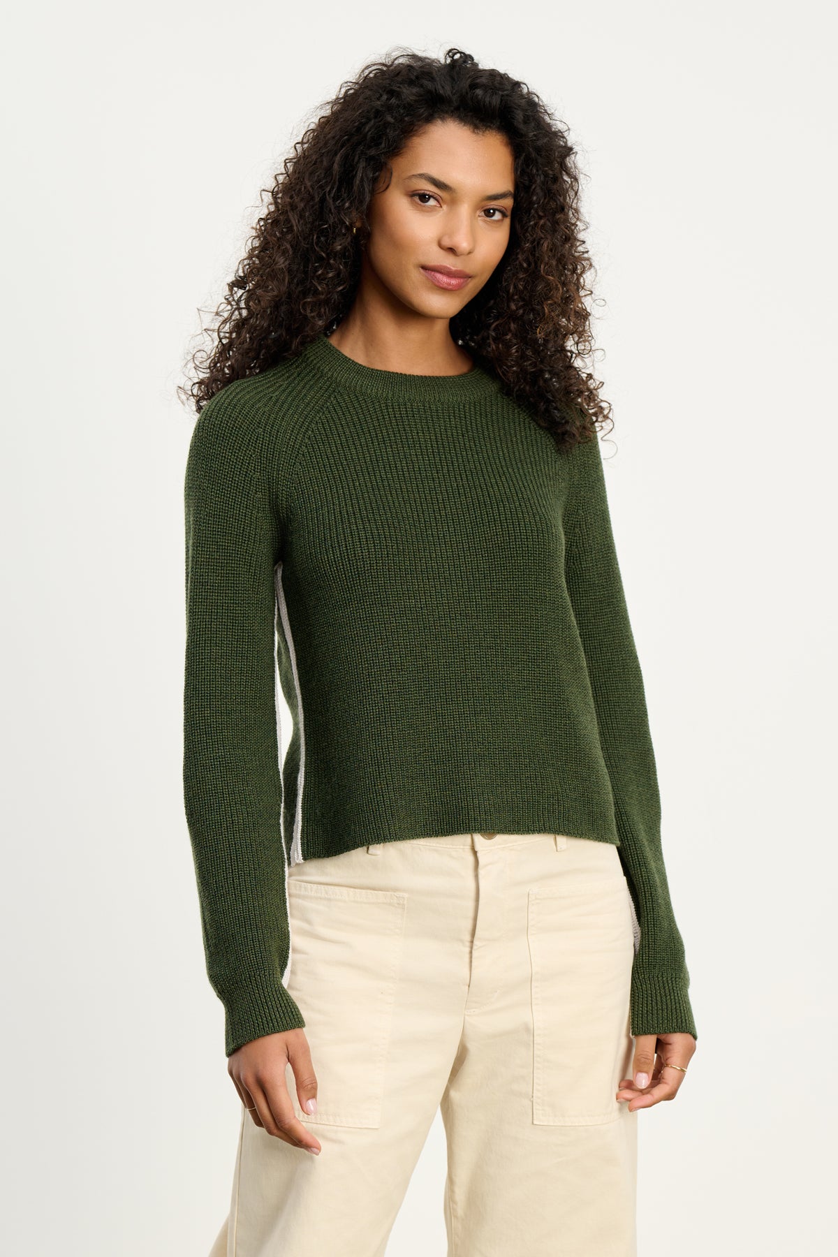 A woman wears the SAVANNAH SWEATER by Velvet by Graham & Spencer, a dark green wool blend, paired with beige pants against a plain white background.-39800362631361